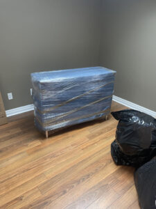 Wrapped wooden dresser being moved by Calgary movers through a narrow hallway.